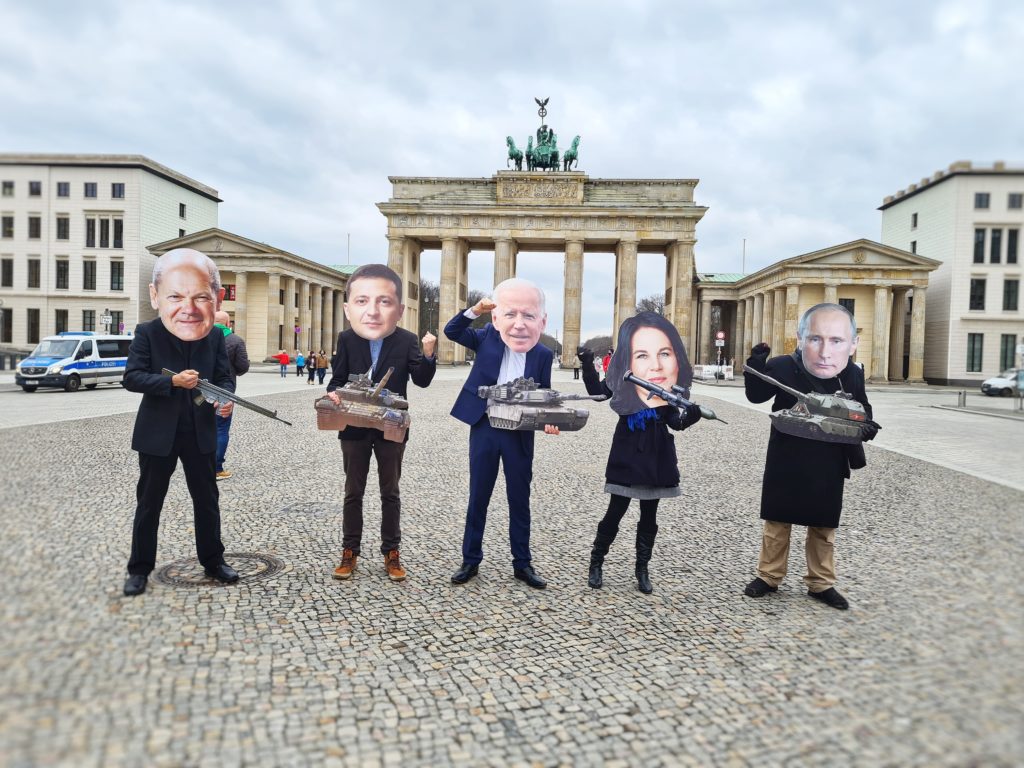 Als Baerbock, Scholz, Selensky, Biden und Putin verkleidete Aktivist*innen posieren mit Spielzeugwaffen vor dem Branenburger Tor